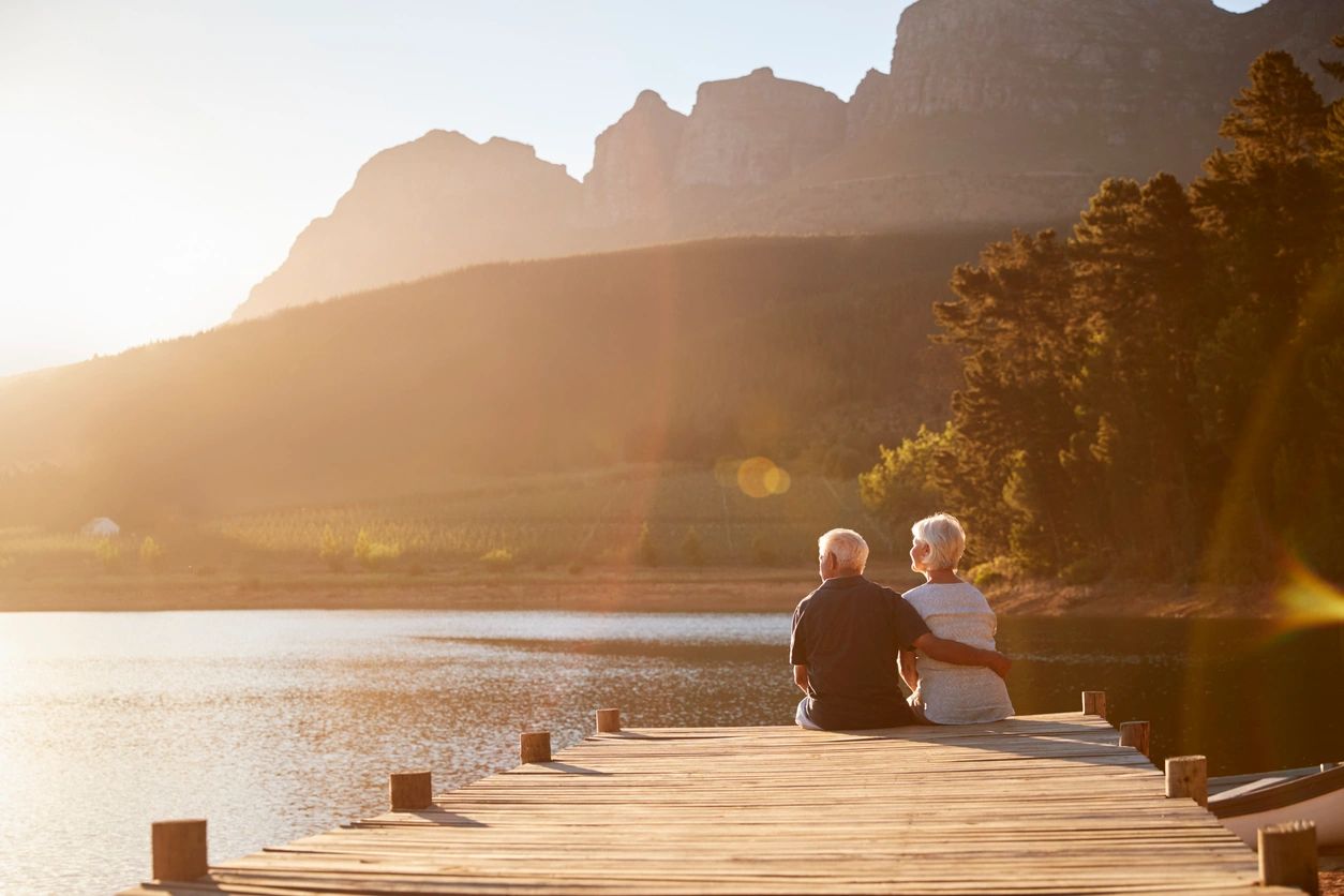 Romantic Senior Couple Sitting On Wooden Jetty By Lake